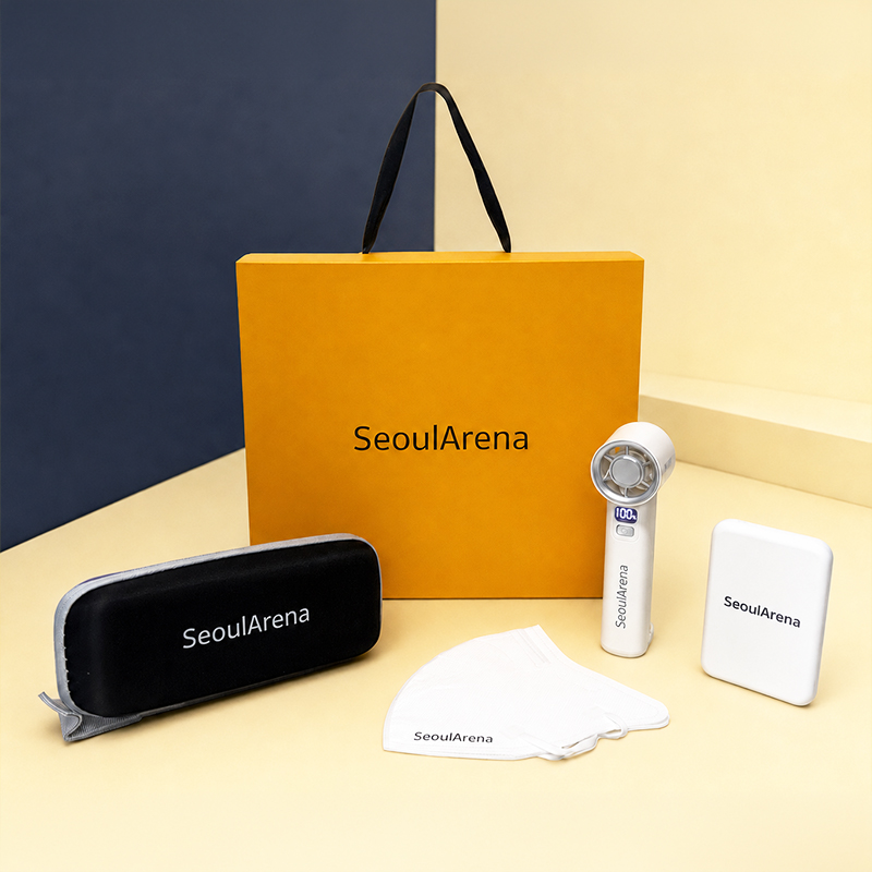 'SeoulArena' 로고가 프린팅된 옐로우 컬러 디자인 그립 슬리브 박스를 중심으로 화이트 맥세이프 보조배터리, 핸디형 터보 포켓팬, 하드 케이스에 담긴 플랫 미니 양우산, KF94 마스크가 정갈하게 구성된 웰컴키트 전체 뷰.