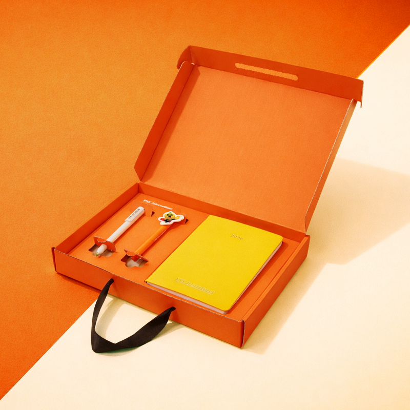 박스를 오픈했을 때의 모습입니다. 선명한 오렌지 박스 내부에 옐로우 톤의 다이어리와 캘린더, 화이트/오렌지 펜이 안정적으로 배치되어 에너제틱한 브랜드 이미지를 전달합니다.