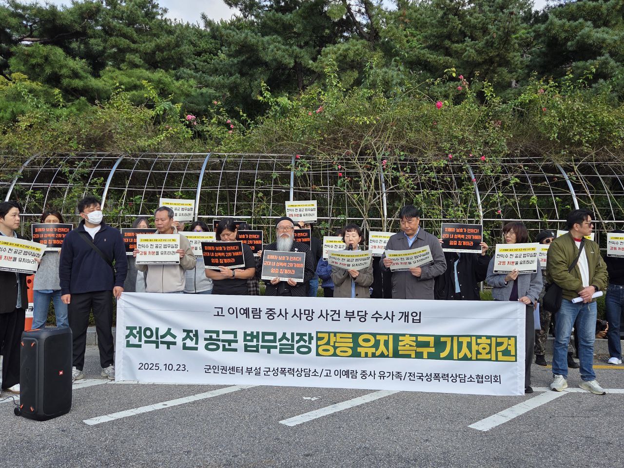 20여 명의 사람들이 현수막을 앞에 두고 피켓을 들고 서 있다. 하얀 현수막엔 '고 이예람 중사 사망 사건 부당 수사 개입 전익수 전 공군 법무실장 강등 유지 촉구 기자회견 2025.10.23. 군인권센터부설 군성폭력상담소 / 고 이예람중사 유가족 / 전국성폭력상담소 협의회'라고 적혀 있다. 사람들이 들고 있는 피켓에는 "피해자 보호가 먼저다! 군대 내 성폭력 2차 가해자 엄중 징계하라", "전익수 전 공군 법무실잘 강등처분을 유지하라!"라고 적혀 있다. 가운데 있는 한 사람이 마이크를 들고 발언하고 있는 모습니다.