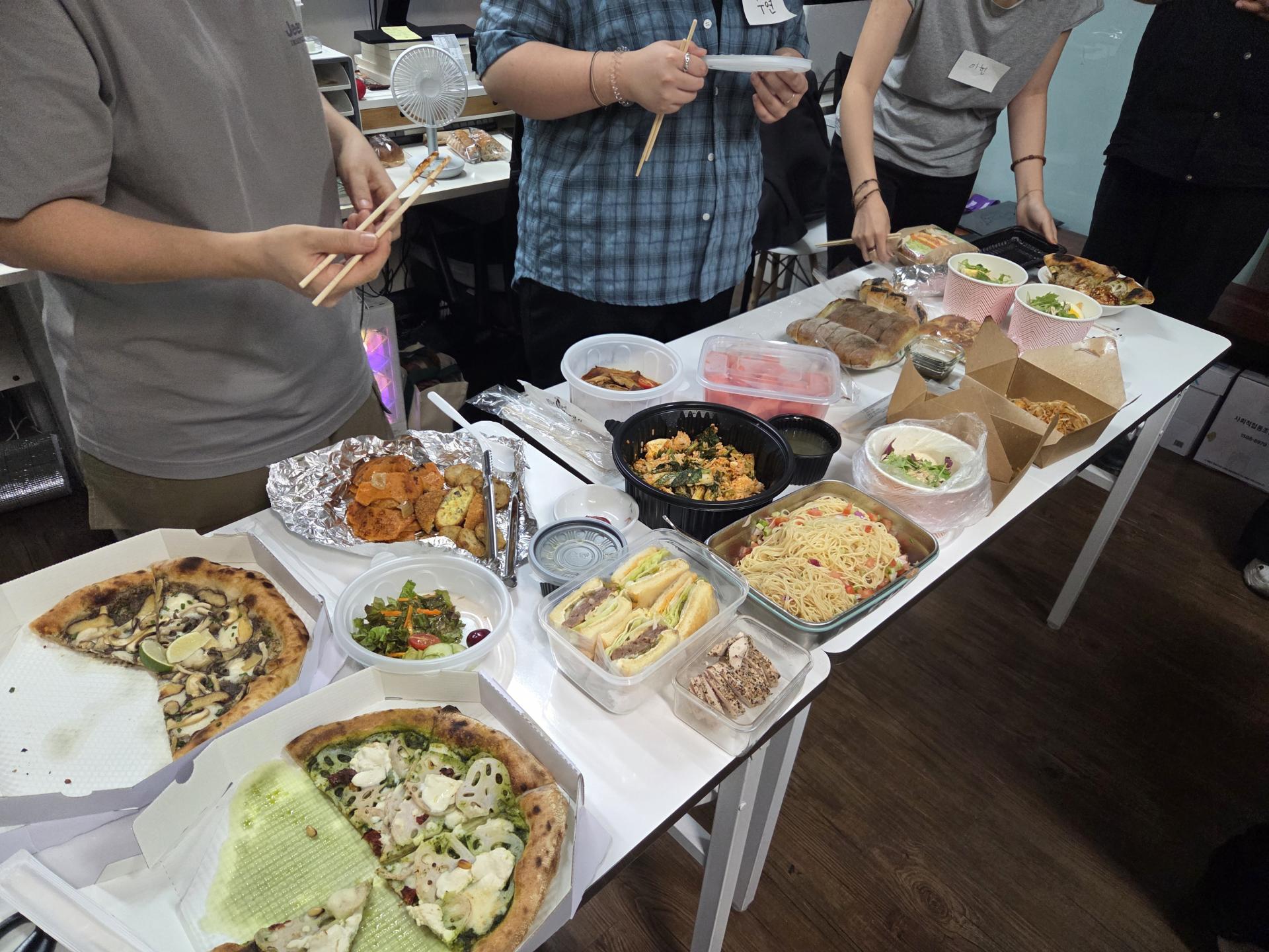 테이블에 놓인 음식과 뒤로는 젓가락을 들고 있는 사람들의 손이 보인다.