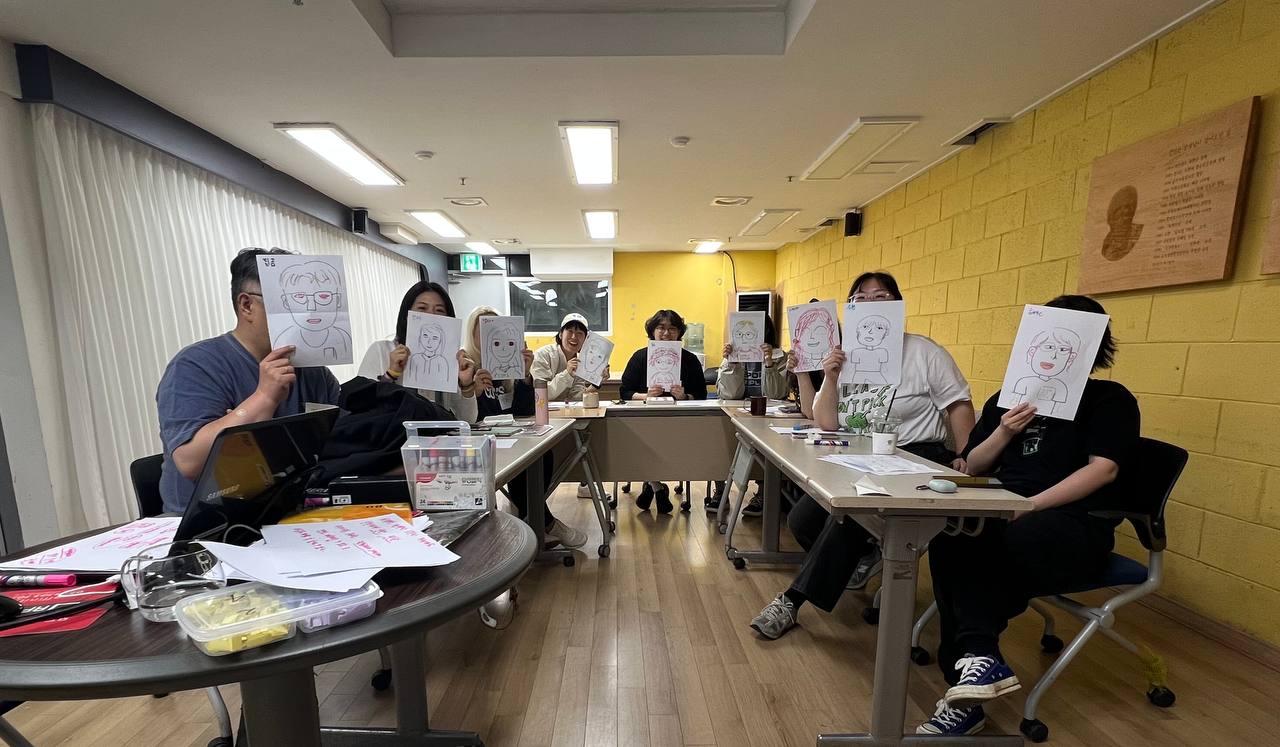 책상에 앉아 자신의 얼굴 그림을 들고 있는 활기단 멤버들의 모습.