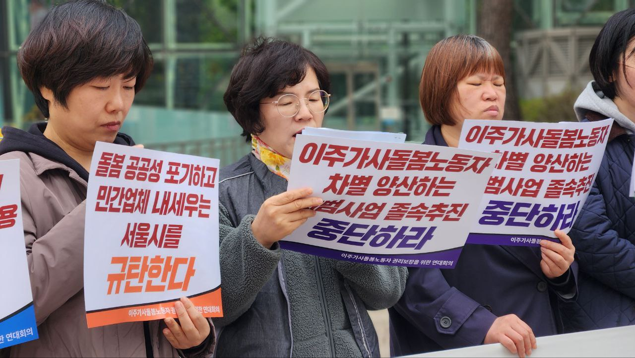 금색테 안경을 쓰고 반곱슬 커트머리의 중장년 여성이 마이크와 피켓을 들고 발언하고 있다.