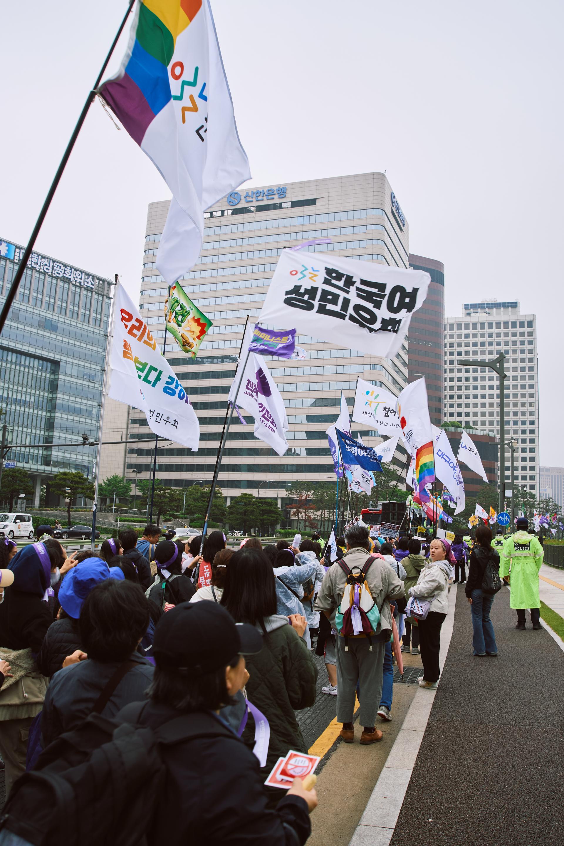 윤석열 파면한 페미니스트 대행진 사진. 많은 사람들이 깃발을 들고 함께 행진하고 있다.