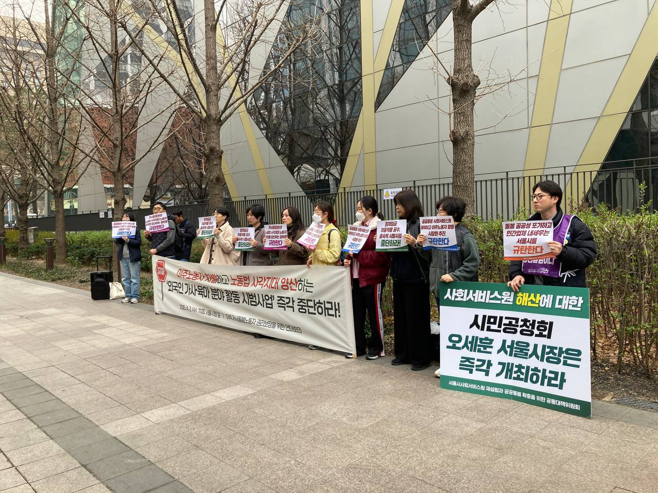 서울시청 화단 앞에 11명의 사람들이 피켓을 들고 현수막 뒤에 서서 시위하고 있다.