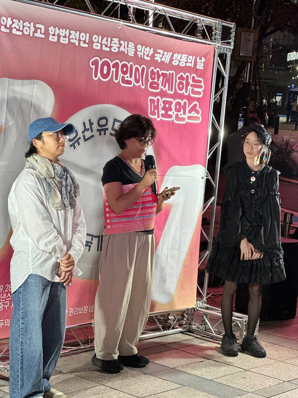 좌측부터 도미님, 정은님, 베라님이 서 있다. 가운데(정은) 참여자는 마이크를 들고 휴대폰을 보며 발언 중이며, 양 옆의 참여자는 순서를 기다리며 발언자의 발언을 경청하고 있다.