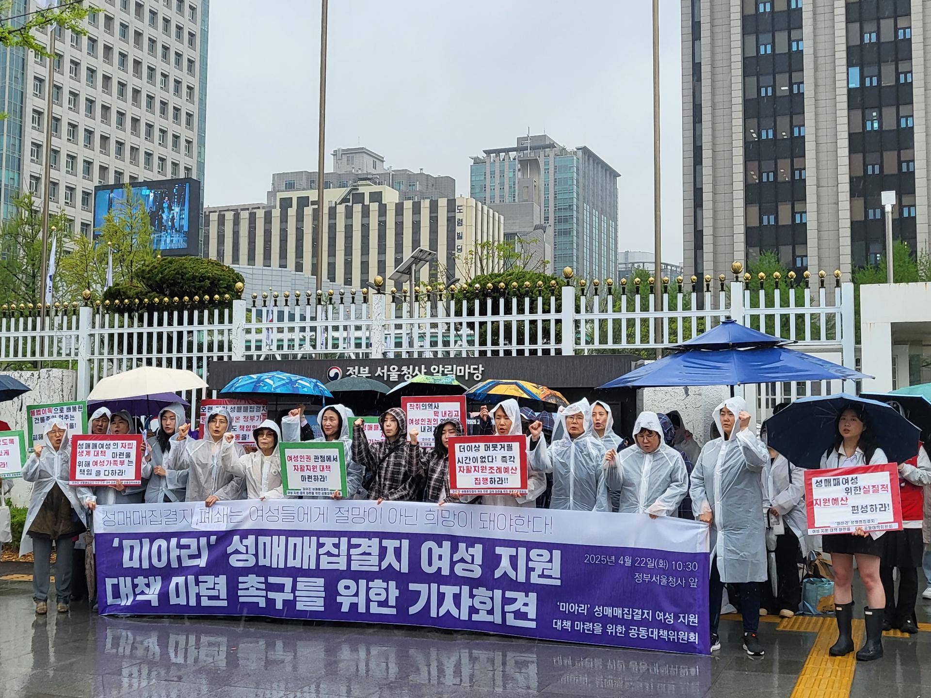 @사진설명: 정부 서울청사 앞에서 열린 기자회견 현장사진. 기자회견 제목이 적힌 현수막 뒤로 활동가들이 '성매매여성의 자립 생계 대책 마련을 위해 여성가족부는 책임을 다하라!', '여성인권 관점에서 자활지원 대책 마련하라!', '더이상 머뭇거릴 시간이 없다! 즉각 자활지원조례 예산 집행하라!!!' 등 문구가 적힌 피켓을 들고 있다. 다같이 구호를 외치고 있다.