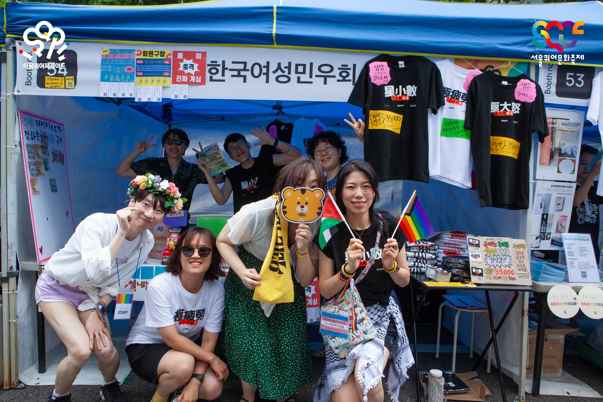 서울퀴어퍼레이드 부스에서 찍은 활동가, 회원 단체 사진. 캐노피에 한국여성민우회가 적힌 현수막이 걸려있고, 테이블에는 프로그램을 진행하기 위한 다양한 물품이 진열되어 있다.