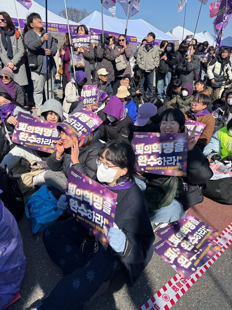 사진 21. 민우회 활동가들이 ‘빛의 혁명을 완수하라!’ 피켓을 들고 환하게 웃으며 기념식(본대회)에 참석하고 있다.