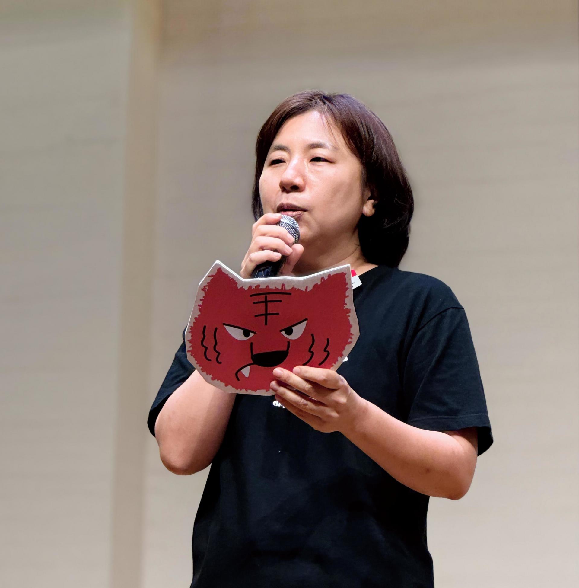 빨간색 호랑이 피켓을 든 사람이 마이크를 들고 뭔가를 말하는 모습 