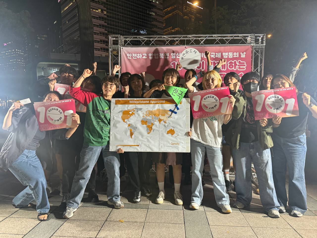 미페프리스톤 승인국가 지도와 한국 깃발, 퍼포먼스 손피켓을 든 민우회 활동가가 현수막 앞에서 단체사진을 찍고 있다. 모두 환하게 웃는 얼굴이다.