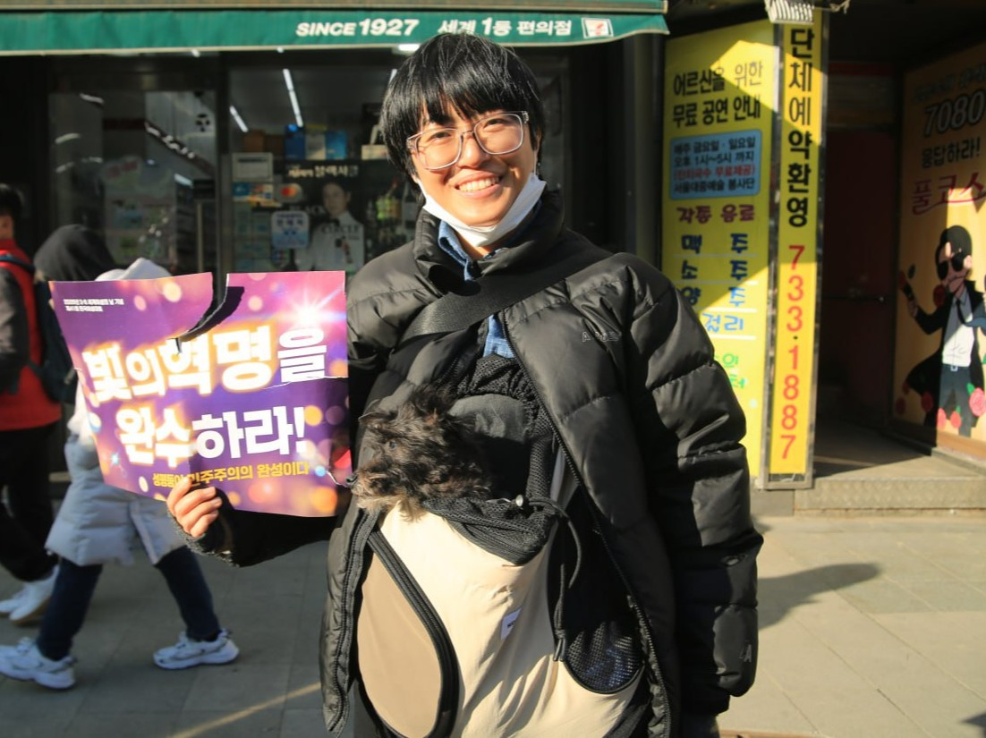 사진 44. 민우회 활동가 행크가 빛의 혁명을 완수하라’라는 피켓을 들고, 반려견 한율과 함께 행진에 참여하고 있다.