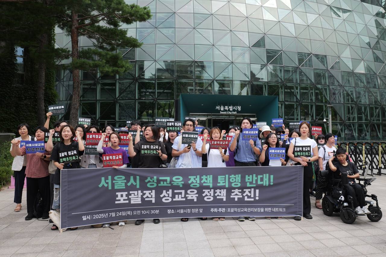 서울시청 앞 많은 사람들이 '서울시 성교육 정책 퇴행 반대! 포괄적 성교육 정책 추진!' 이라고 쓰인 현수막 뒤에서 피켓과 주먹을 들고 구호를 외치고 있는 사진.