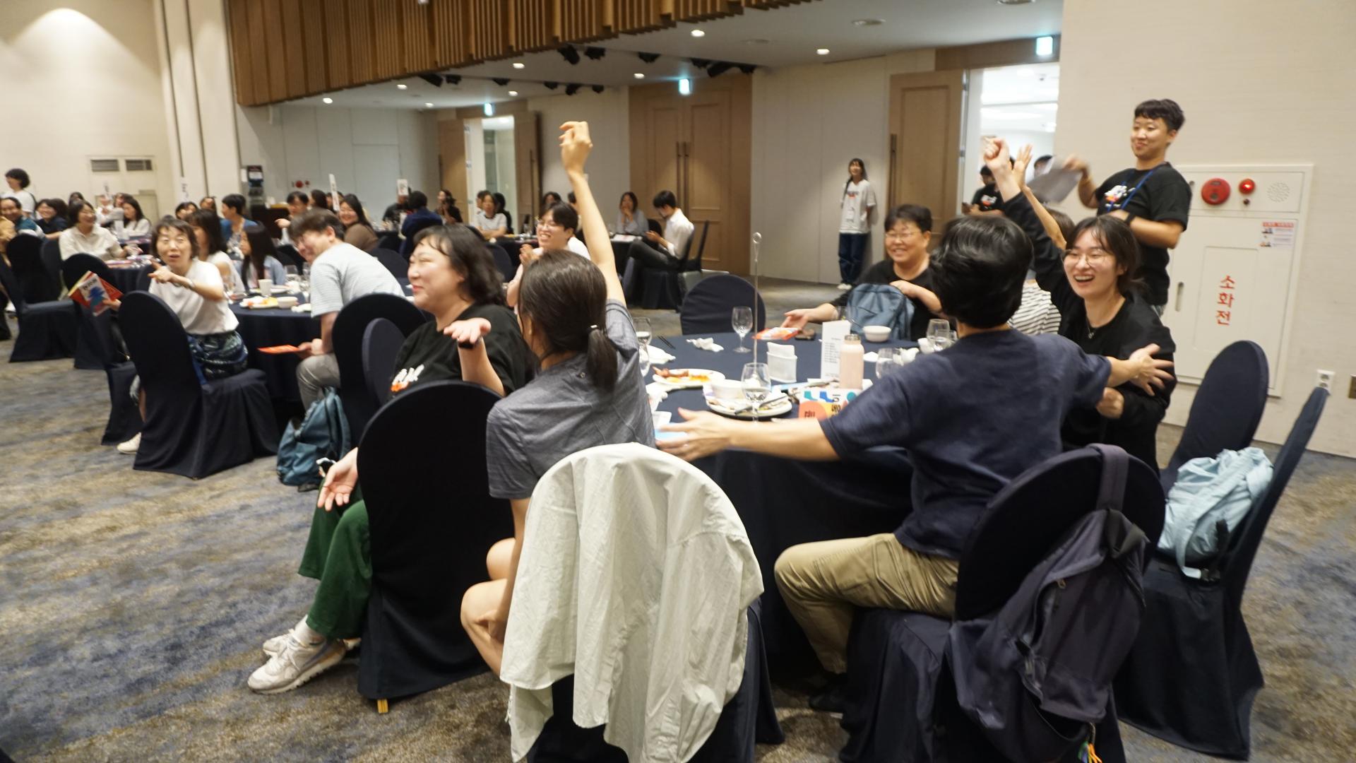 한 원형테이블의 사람들이 너도나도 한 손을 높이 들고 서로를 바라보며 웃고 있는 모습.