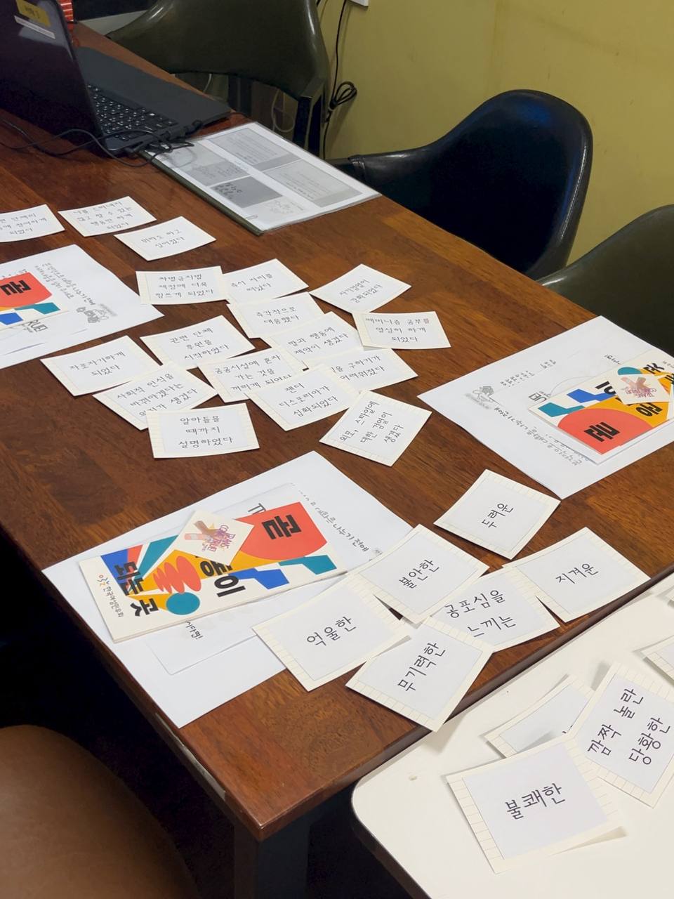 테이블에 놓인 감정 및 행동 영향카드의 모습. 억울한, 불안한, 두려운, 무기력한, 공포심을 느끼는, 지겨운, 불쾌한 등의 감정 카드가 놓여 있고 그 위로 자포자기하게 되었다, 알아들을 때까지 설명하였다, 외모에 대한 검열이 생겼다 등의 행동 카드가 놓여 있다