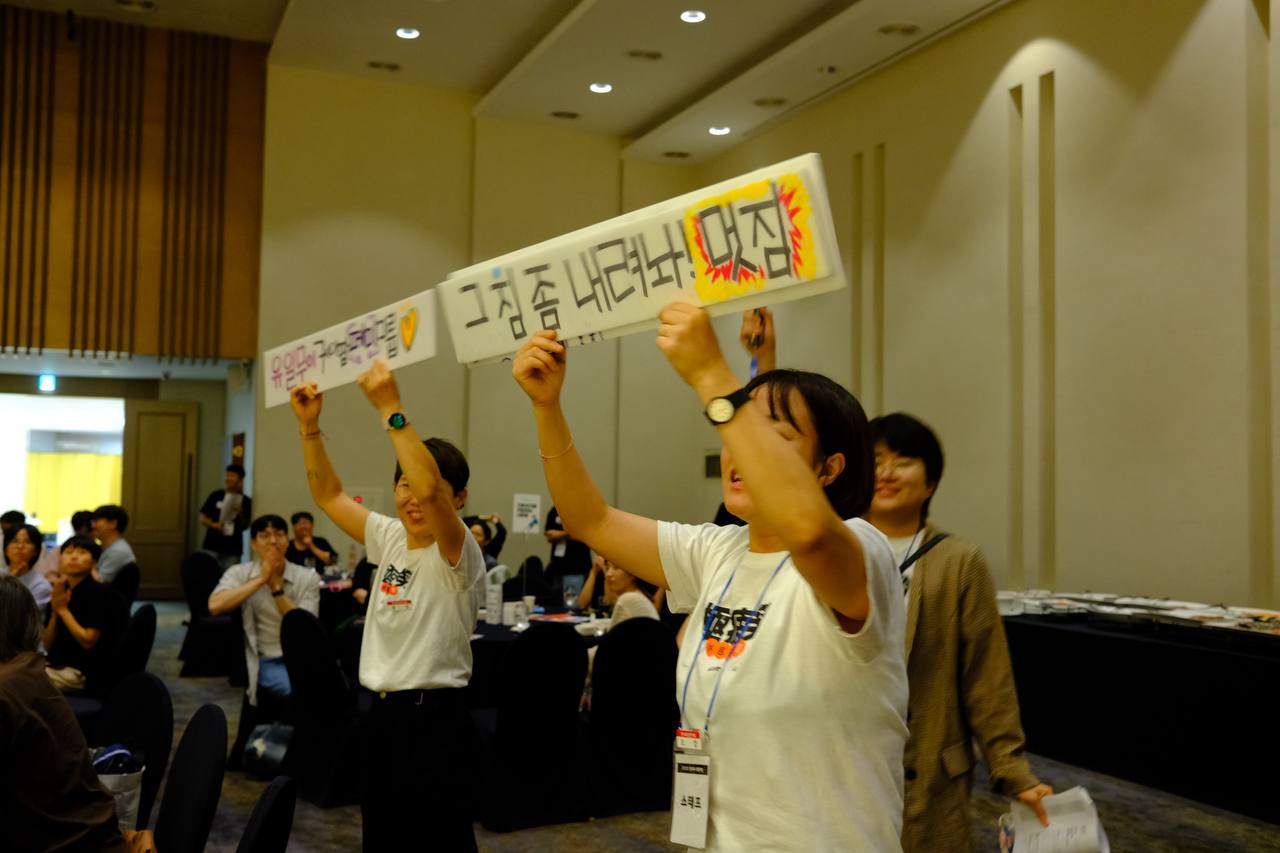 공연팀을 향해 환호하며 피켓을 든 두 사람의 모습. "유일무이 케이팝 페미그룹 (하트)", "그 짐 좀 내려놔! 멋짐"이라고 쓰여 있다. 