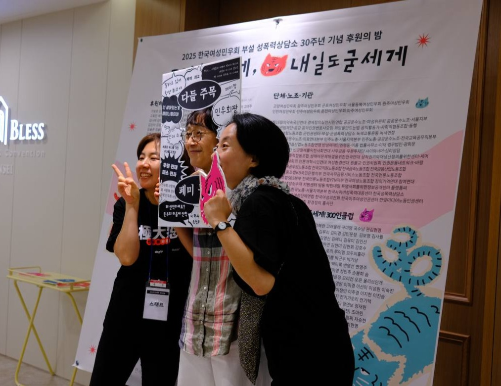활동가 명단이 빼곡히 적힌 행사 현수막을 배경으로 세 명의 사람이 사진을 찍고 있다. 그 중 한 명은 사람 얼굴 정도 크기의 분홍색 호랑이 얼굴 피켓을 들고 있고, 가운데 서 있는 한 명은 "다들 주목", "페미 등장" 등 호들갑스럽게 이목을 끄는 문구들이 빽빽히 적혀 있고 가운데 뚫린 곳에 얼굴을 넣고 사진을 찍을 수 있는 우드락 피켓을 들고 있다. 나머지 한 명은 브이를 그리고 있다. 셋 다 앞쪽 다른 카메라를 보고 있는 모습이다. 
