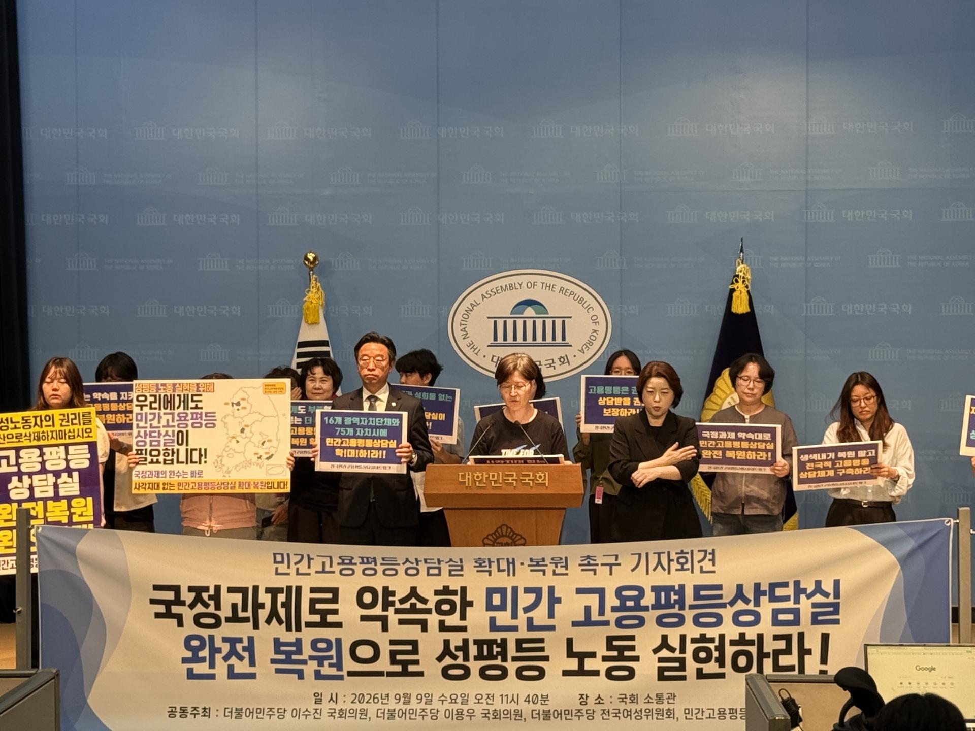 국회 소통관에서 여러명의 국회의원과 활동가들이 기자회견을 하고 있다. 푸른색 배경에는 국회 로고가 있고 전면 아래 현수막에는 기자회견 제목 '국정과제로 야곡한 민간 고용평등상담실 완전 복원으로 성평등 노동 실현하라!' 라고 적혀있다