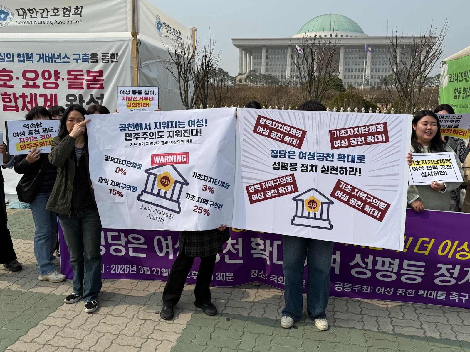 공천에서 지워지는 여성! 민주주의도 지워진다! 8회 지방선거 결과 여성 비율 왼쪽 피켓엔 "광역자치단체장 0%", "기초자치단체장 3%", "광역지역구의원 15%", "기초지역구의원 25%"라고 써있고, 오른쪽 피켓엔 "광역자치단체장 여성공천확대", "기초자치단체장 여성공천확대", "광역지역구의원 여성공천확대", "기초지역구의원 여성공천확대"라고 써있다.