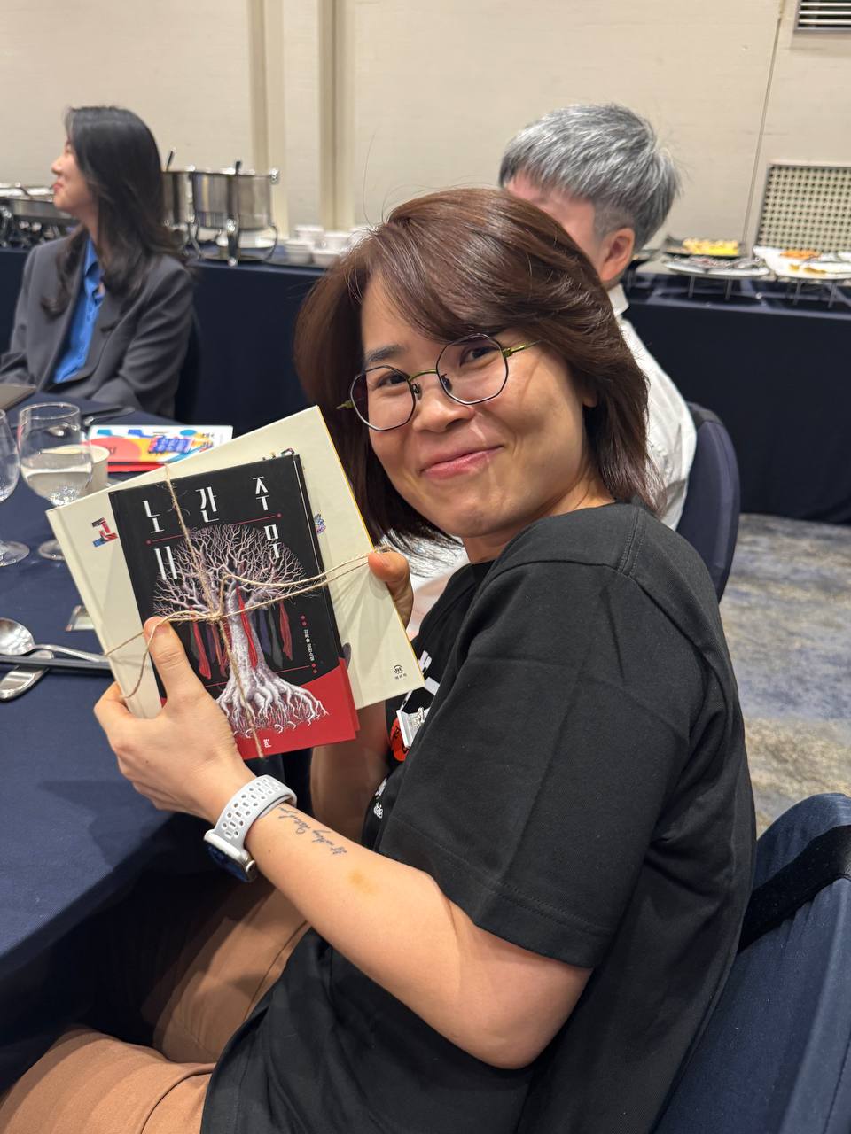 책 '노간주나무'를 들어보이며 카메라를 향해 웃어보이는 한 사람의 모습.