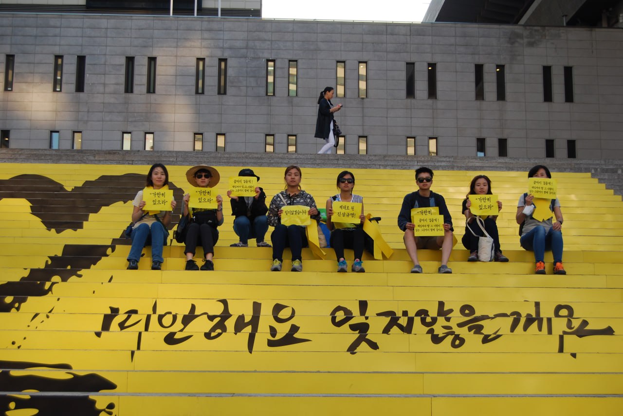 세월호 미안해요 잊지않을게요 계단에 앉아 카메라를 바라보고 있는 활동가들의 모습