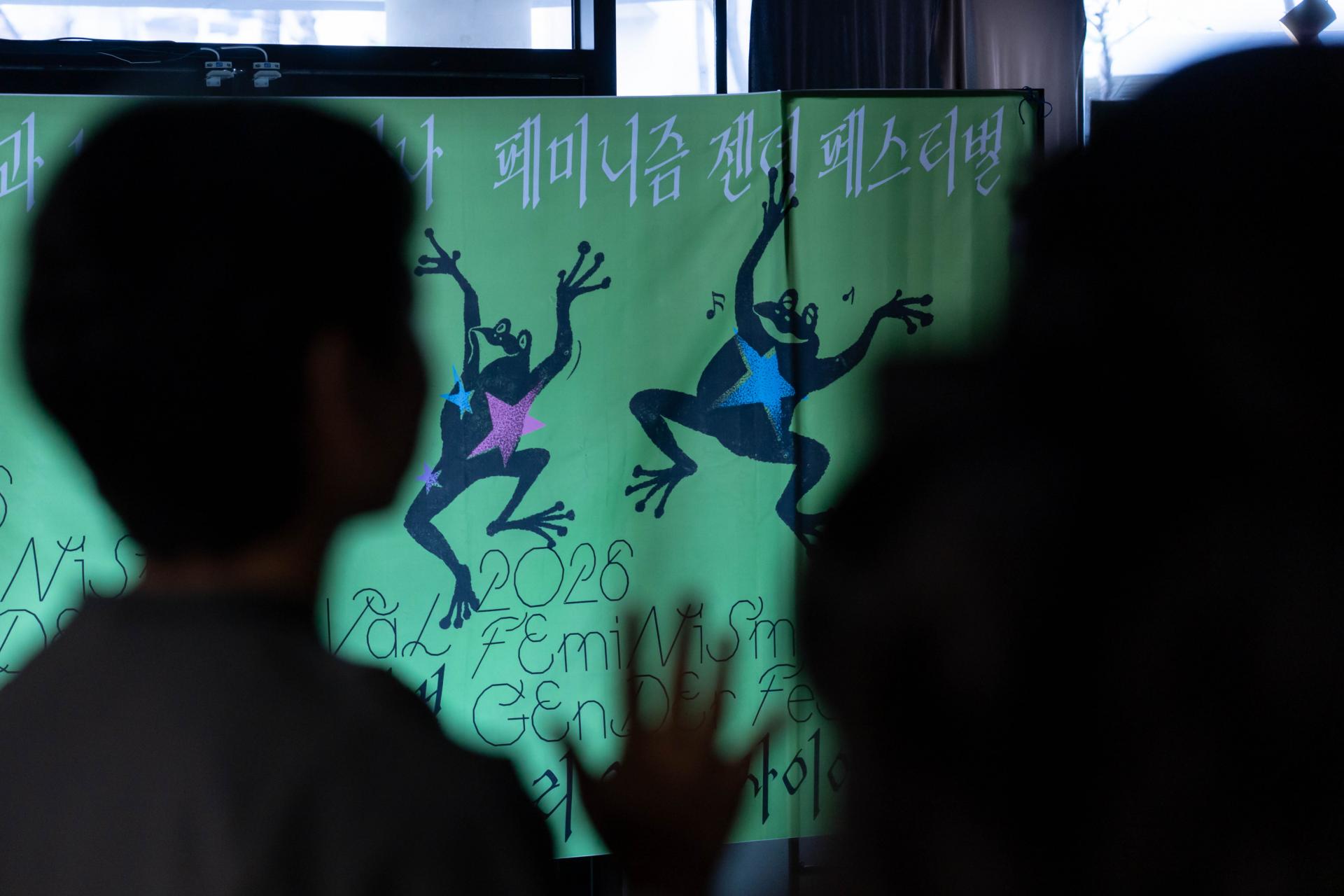 페미니즘 젠더 페스티벌이라고 적힌 현수막 앞쪽으로 사람들의 그림자가 찍혀 있다