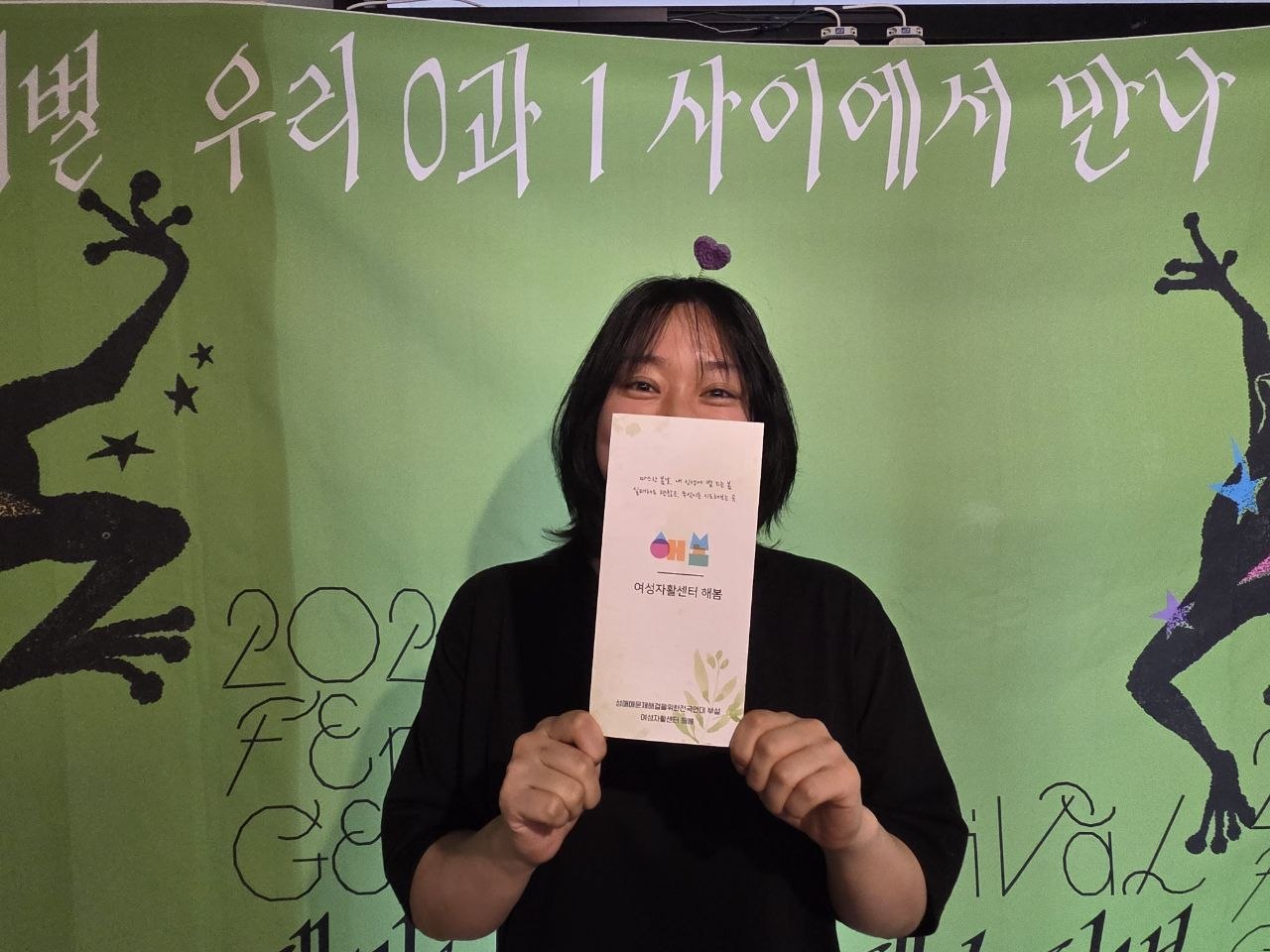 리플렛을 들고 수줍게 웃어 보이고 있는 참여자의 모습