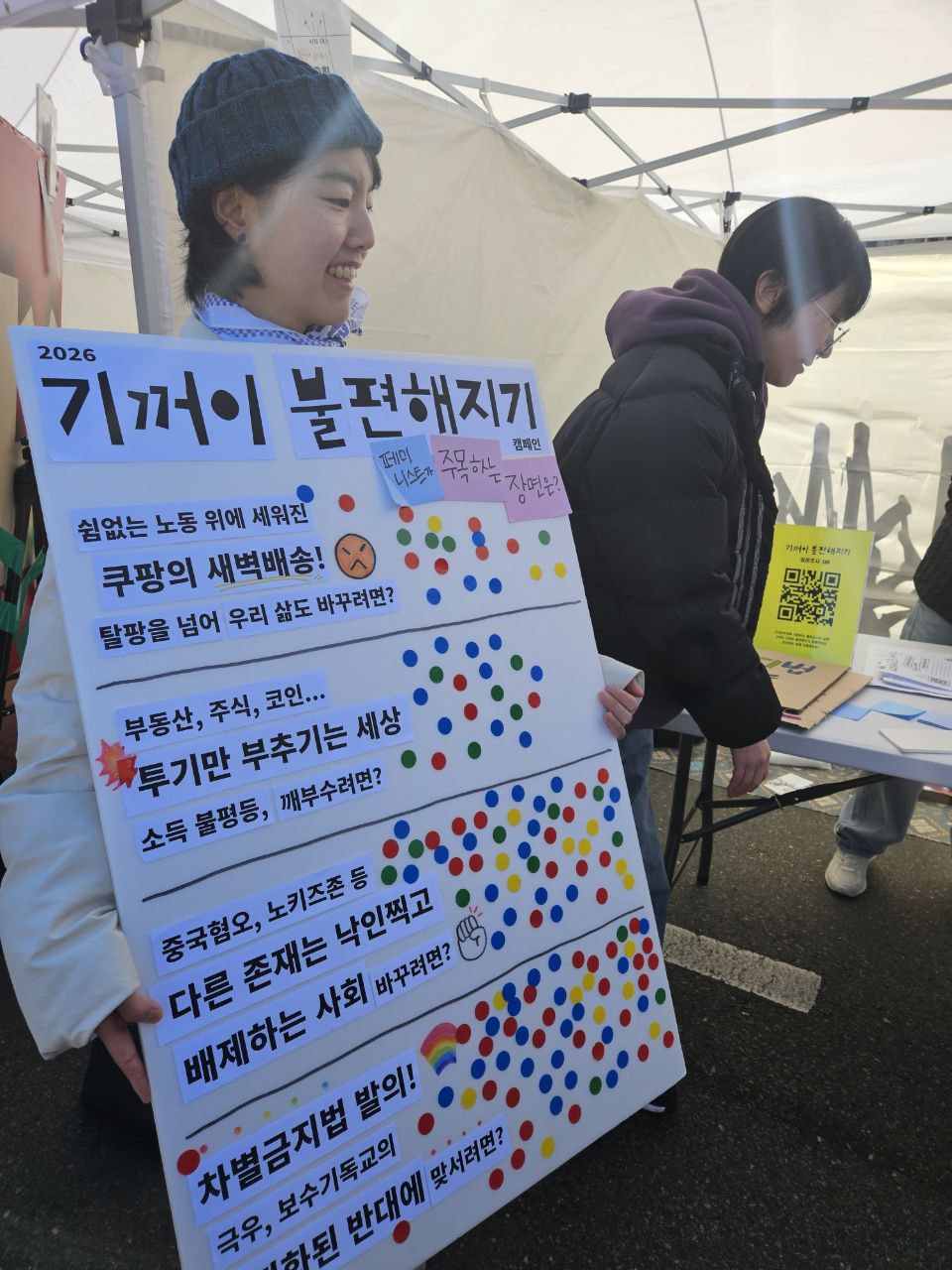 사진 3. 민우회 활동가 제이와 다혜가 기꺼이 불편해지기 설문조사를 위한 판넬을 들고 있다. 문제적 장면 4가지에 골고루 스티커가 붙여져있다.