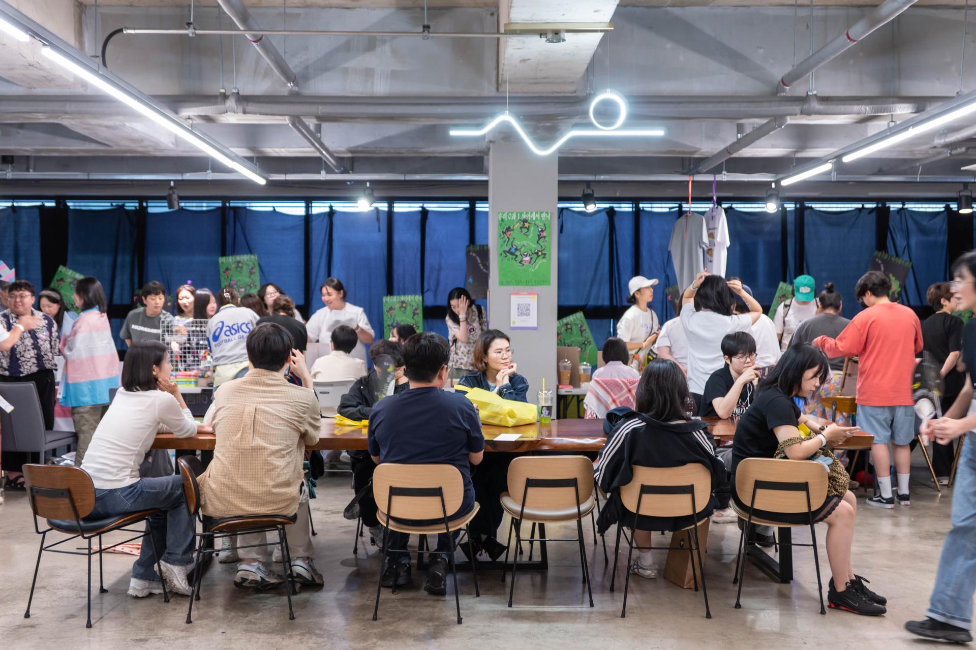 약 9명의 사람들이 휴식존에서 휴식을 취하고 있다. 그 뒤로는 부스에 참여하는 사람들과 운영자들이 여럿 얽혀있다