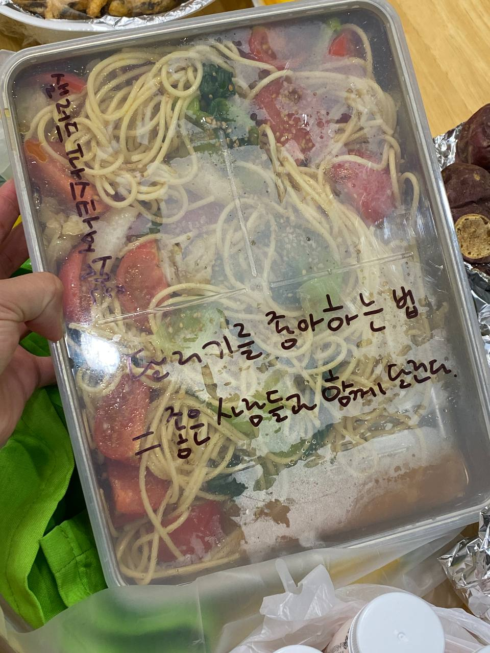 샐러드 파스타가 담겨있는 통. 통의 뚜껑 왼쪽 상단에는 "샐러드 파스타"라고 작성되어 있고, 하단 중앙에는 "달리기를 좋아하는 법=좋은 사람들과 함께 달린다"라고 작성이 되어있다.