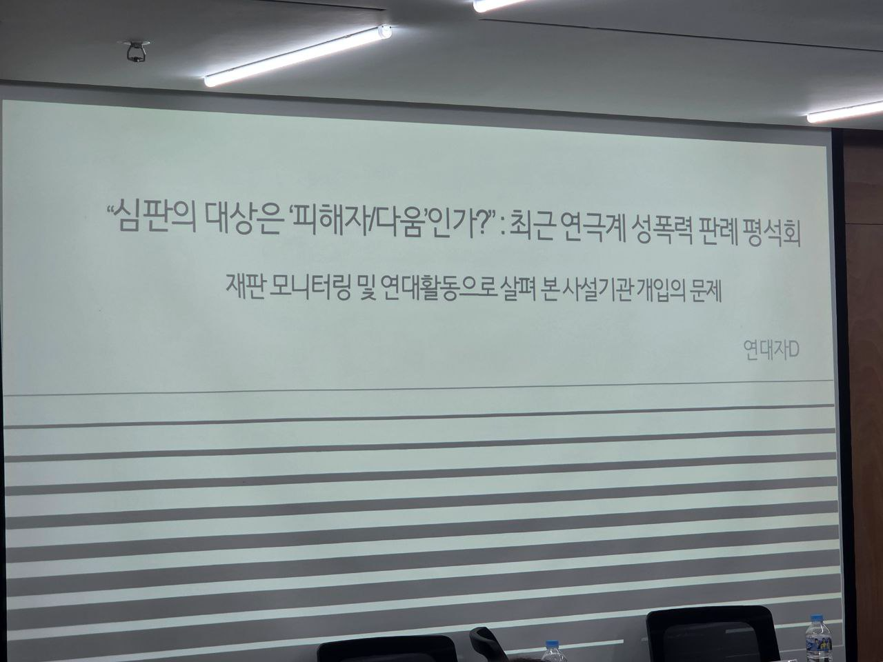 스크린에 "〈심판의 대상은 "피해자/다움"인가?: 최근 연극계 내 성폭력 판례 평석회〉 재판 모니터링 및 연대활동으로 살펴본 사설기관의 개입의 문제'라고 발표문 제목이 쓰여있고, 하단에 검은색 선이 줄무늬처럼 디자인되어 있는데, 아래로 내려갈수록 점차 굵어진다.