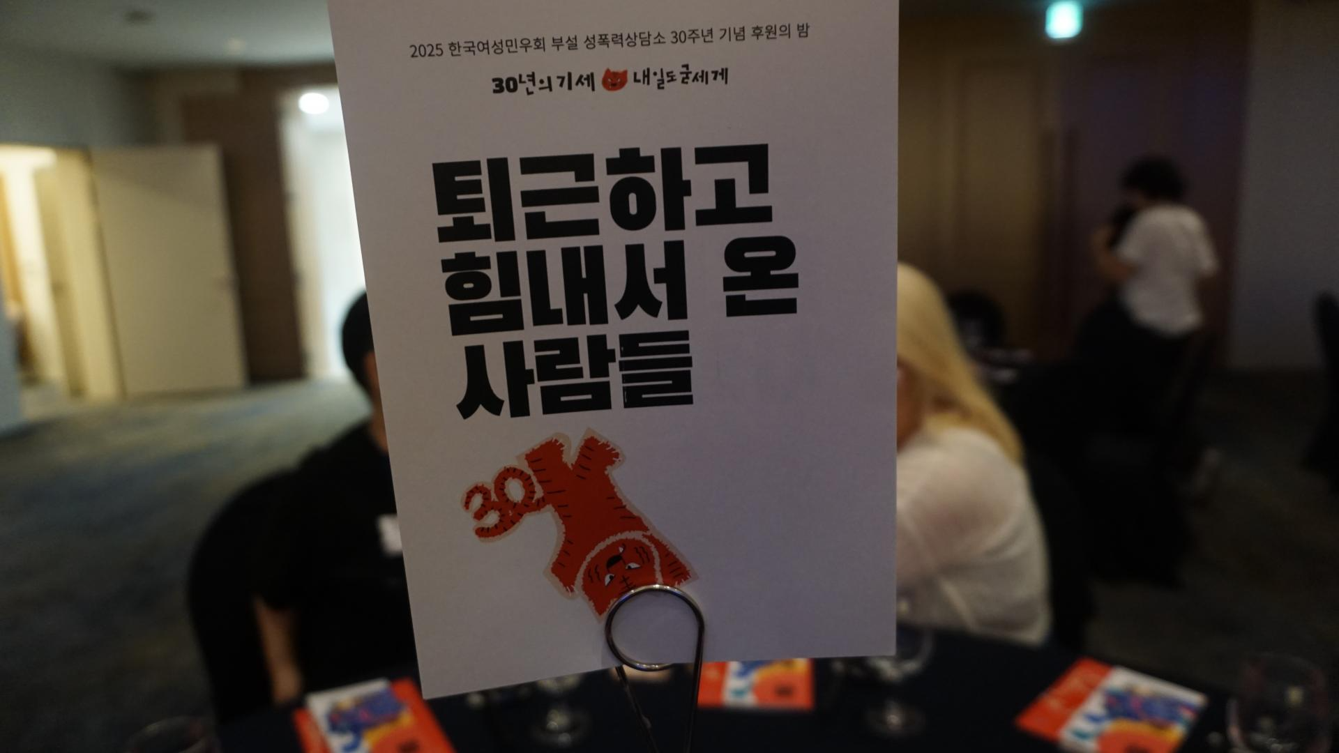 행사장 테이블 위 팻말: '퇴근하고 힘내서 온 사람들'. 빨간색 호랑이가 거꾸로 선 이미지가 들어가 있다.