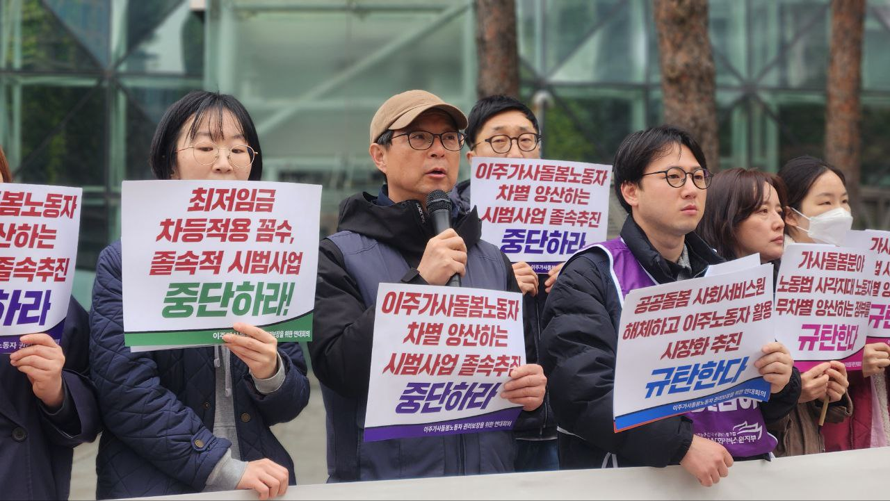 황토색 캡모자를 쓰고 검은색 테 안경을 쓴 장년 남성이 마이크와 피켓을 들고 발언하고 있다.