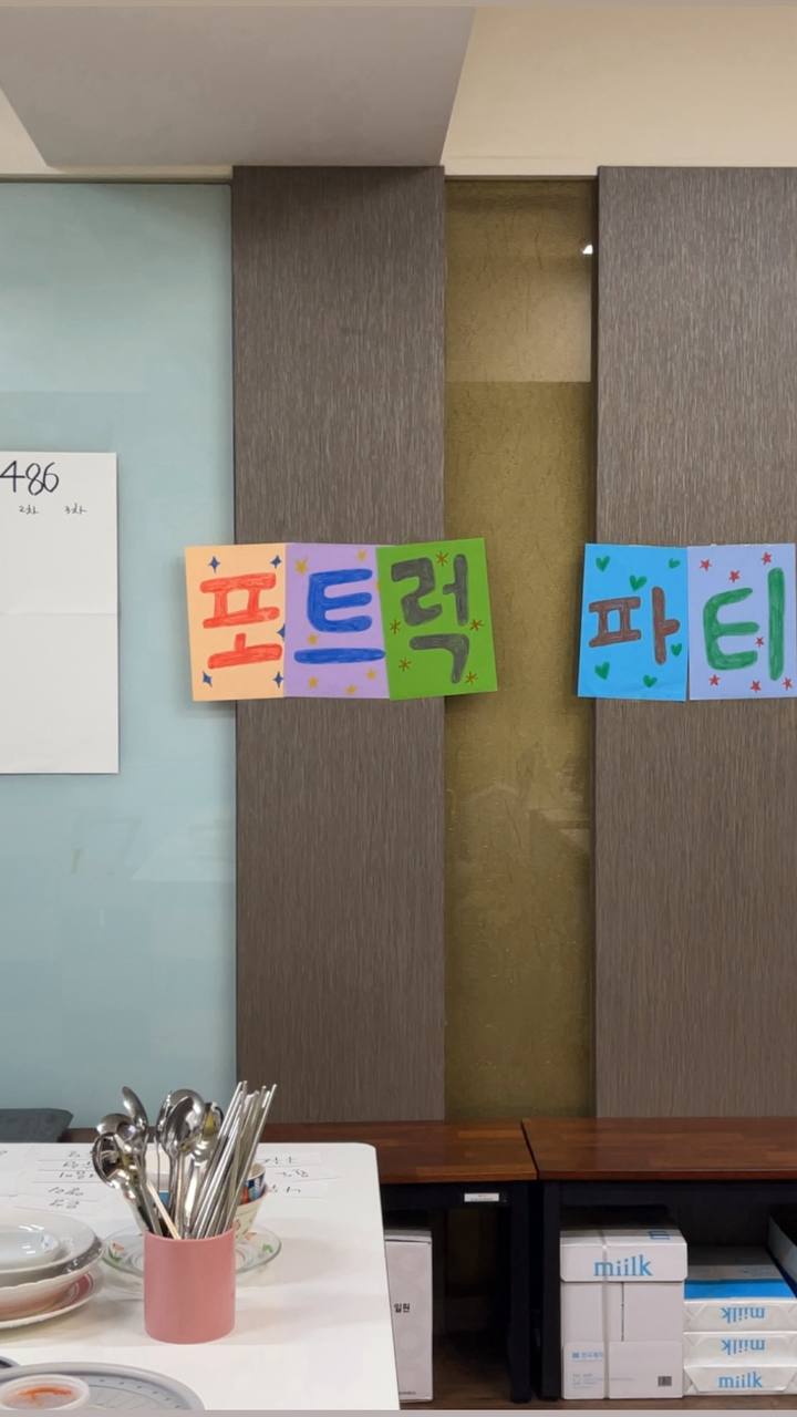 '포트럭 파티'가 적힌 종이가 벽에 붙어 있고, 테이블에는 수저와 접시가 놓여져 있다.