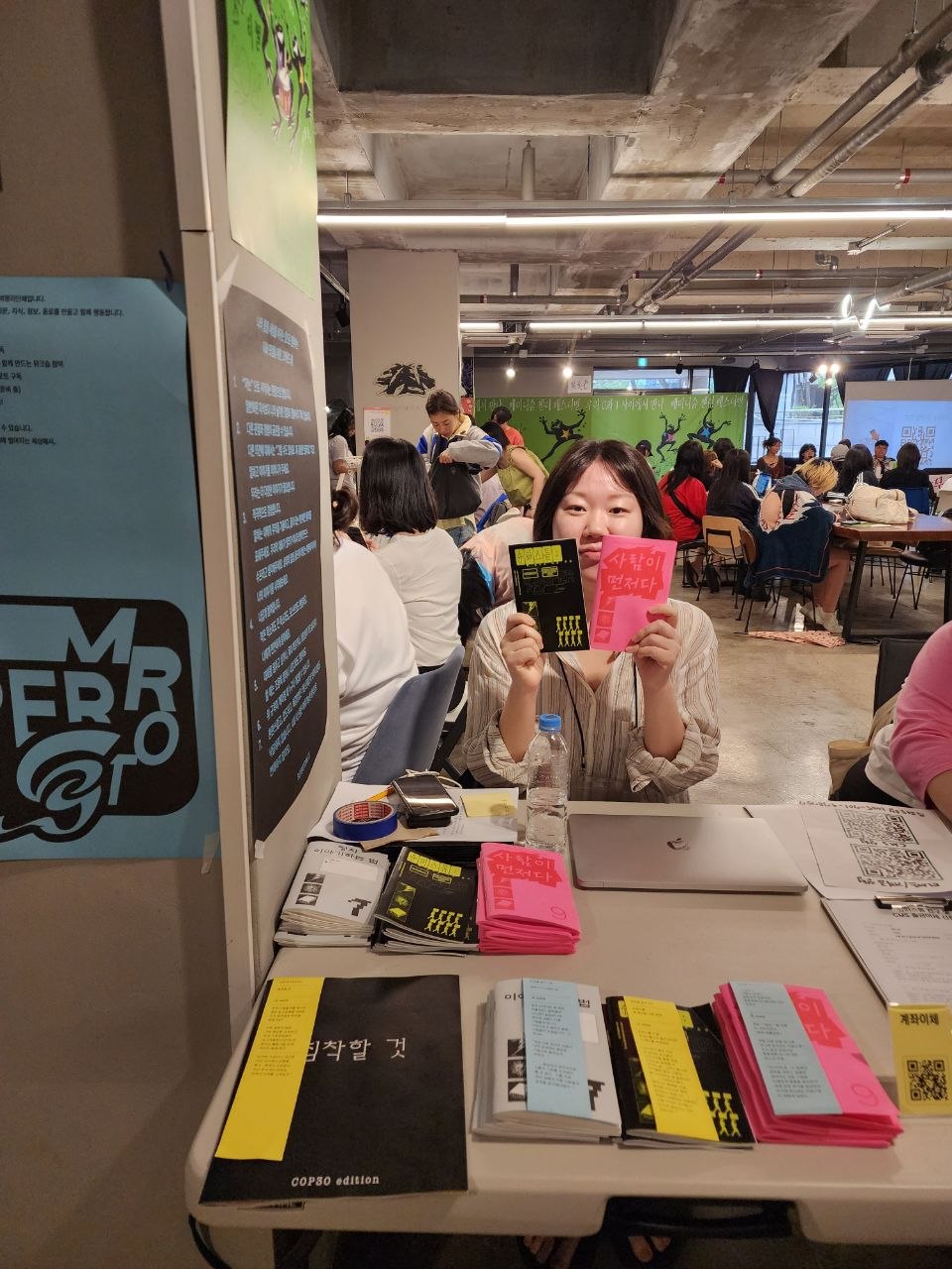 부스 앞에서 가지고 온 진 두 권을 들고 카메라를 바라보고 있는 슈퍼스톰 부스 운영자들의 모습
