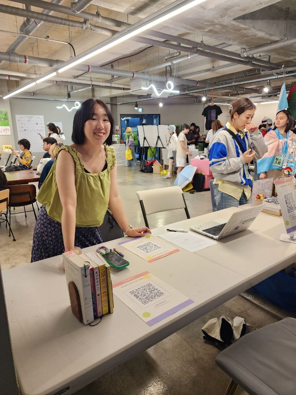 부스 앞에 선 채로 환히 웃고 있는 쓰리썸플레이스 부스 운영자의 모습