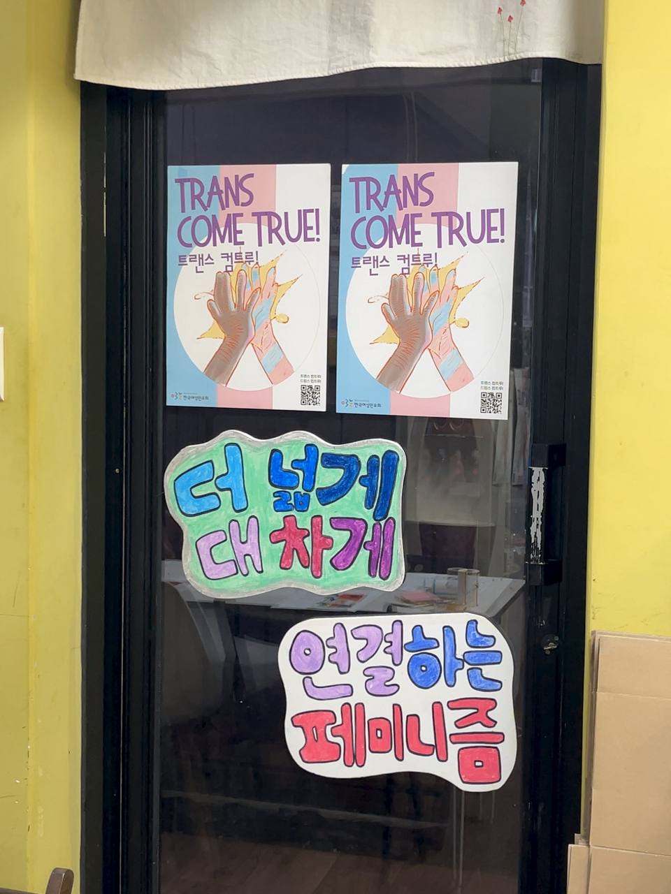 유리문에 트랜스 컴트루 포스터 아래로 더 넓게 대차게, 연결하는 페미니즘이라고 적힌 피켓이 붙어 있다