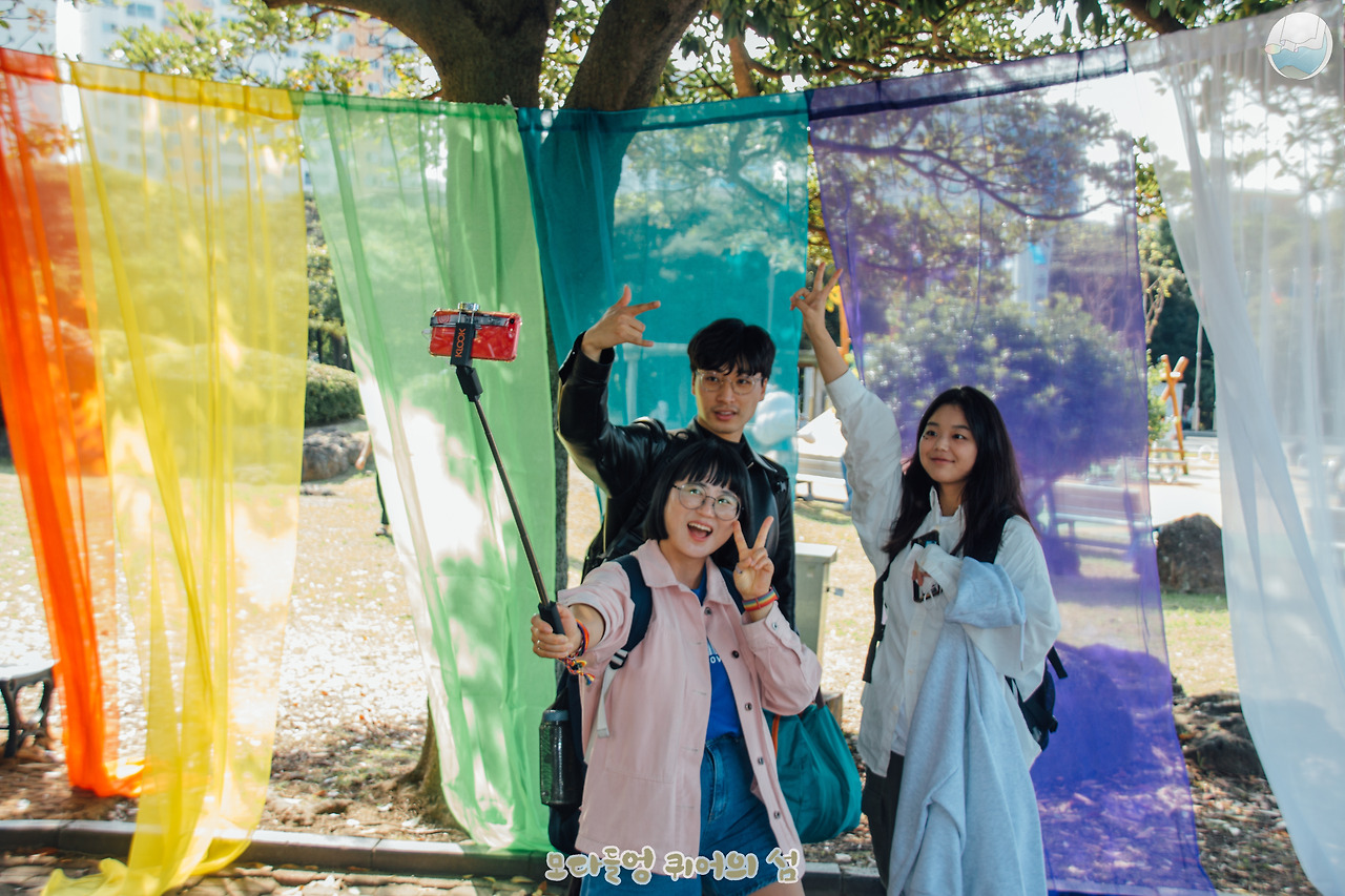 무지개 커튼을 배경으로 셀카 촬영중인 춘천퀴어문화축제 조직위의 모습.