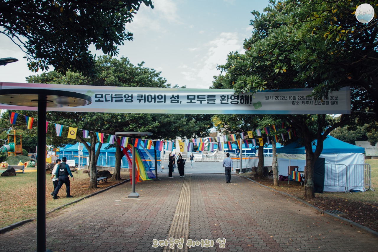 행사 준비가 진행중인 신산공원의 모습. 프라이드 플래그로 만들어진 퀴국기와 함께 무지개 커튼 그리고 '모다들엉 퀴어의 섬, 모두를 환영해!'라고 쓰여진 플래카드가 내걸려있다.