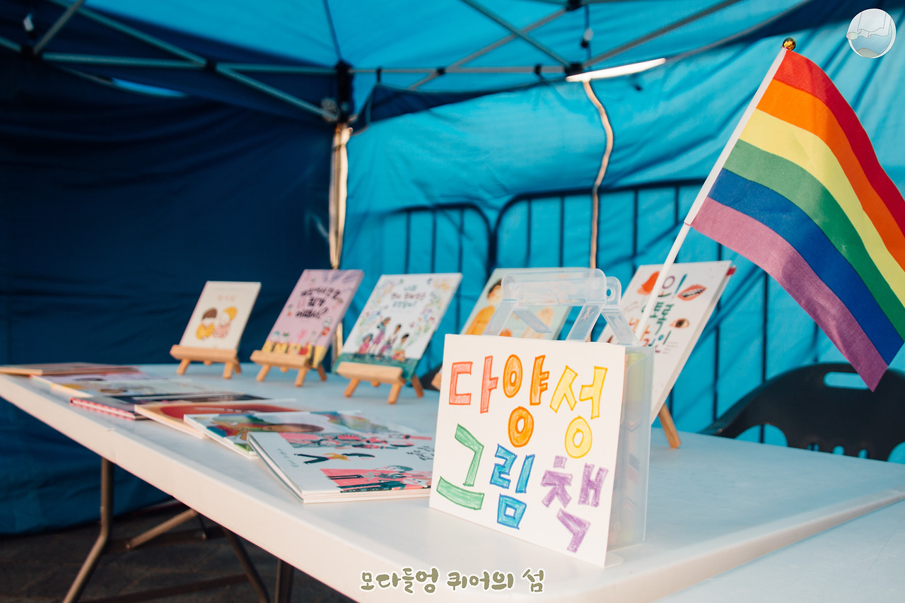 전교조 제주지부 여성위원회 준비위 부스에서 진열되어 있는 다양성 그림책들. 부스 테이블 한편에 무지개 깃발이 꽂혀있다.