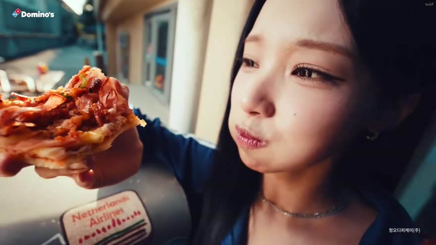피자를 먹는 인물 클로즈업. 뒤쪽에 옛 항공사 스티커가 붙은 트렁크가 놓여 있다