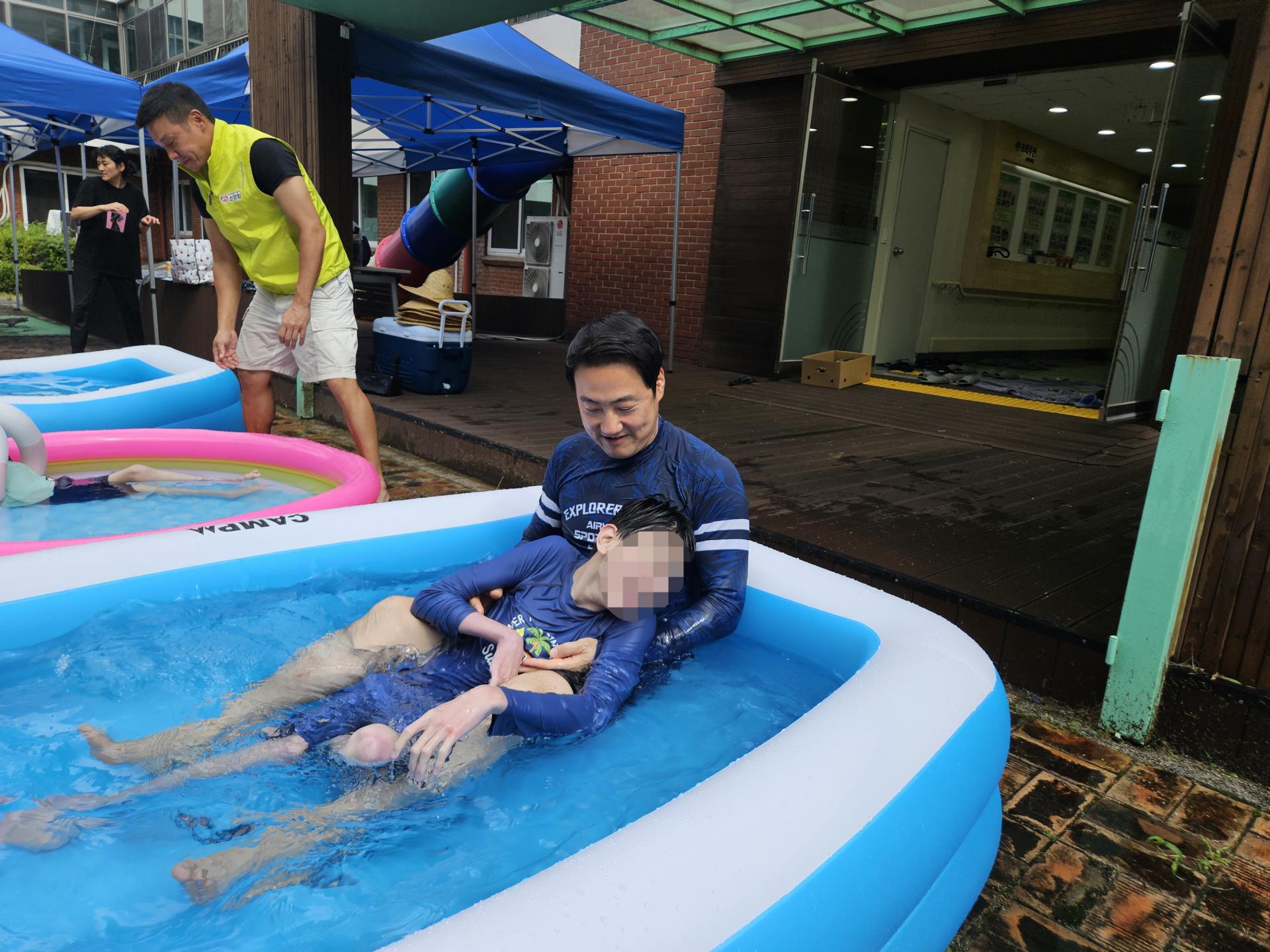 작은풀장에서 여유롭게 물을 즐기는 이용자와 봉사자