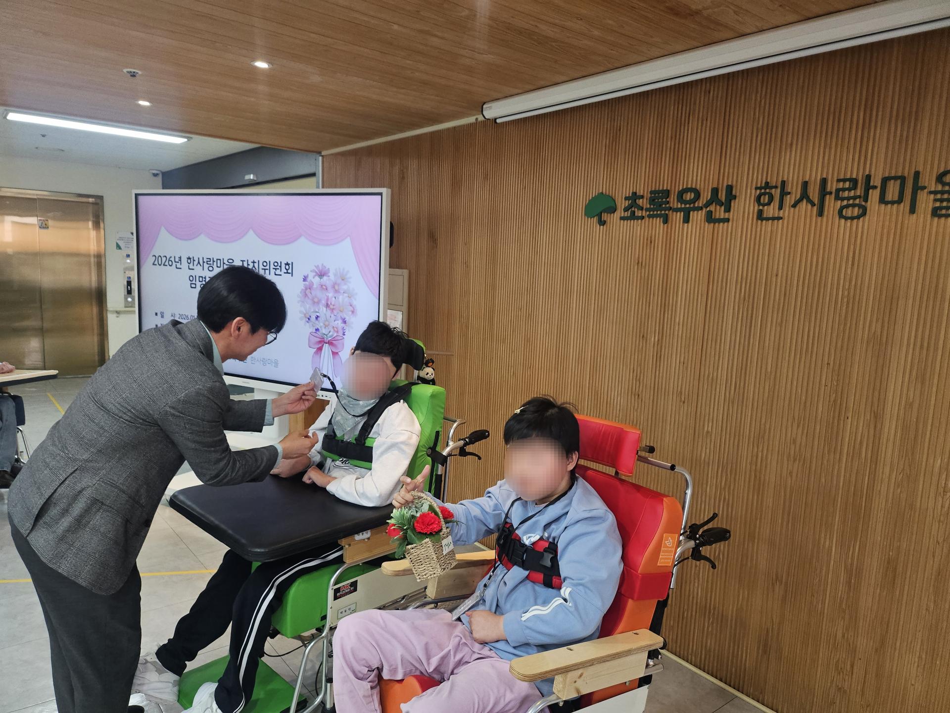 위원증과 꽃바구니를 받는 이용자와 전달하는 원장님