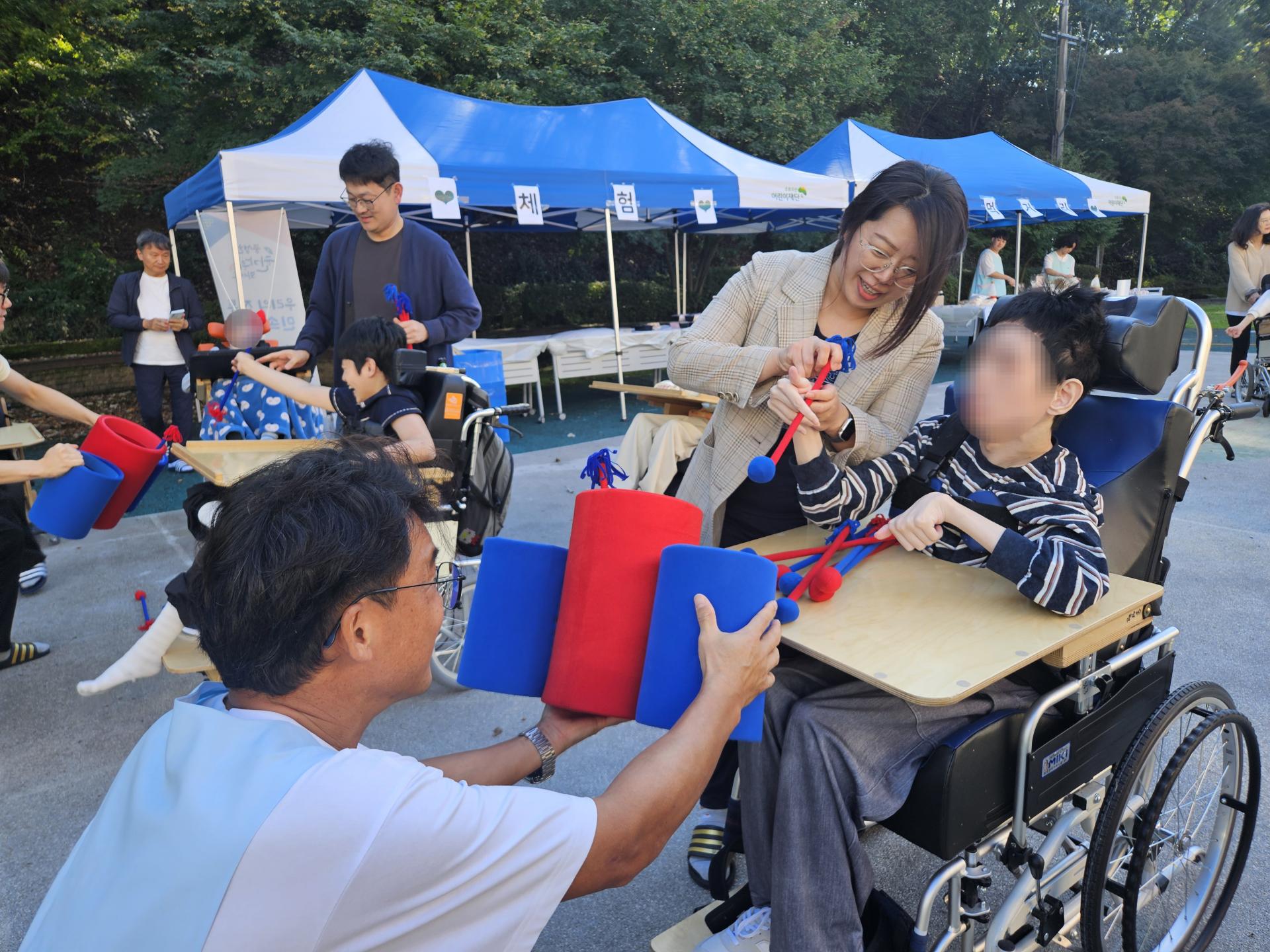 투호를 던지는 이용자와 봉사자 그리고 넣기 쉽게 통을 잡아주는 선생님