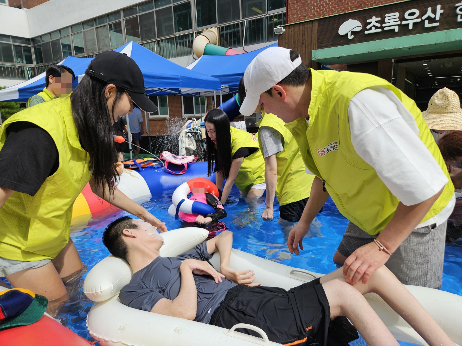 큰 풀장에서 물놀이를 하며 즐거워하는 이용자와 봉사자