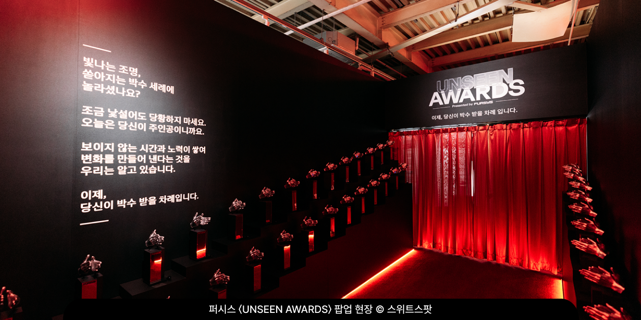 퍼시스 〈UNSEEN AWARDS〉 팝업 내부, 박수 치는 손 모양 트로피가 줄지어 놓인 레드카펫 통로와 방문객에게 건네는 메시지 벽면