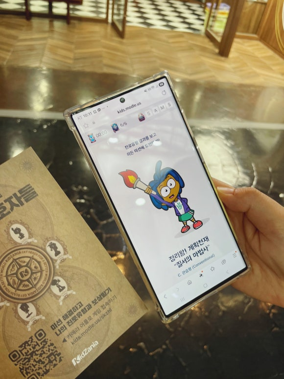 <img src="SE-a0e9f897-1a5f-4862-8232-a380f94343c0.jpg" alt=“핸드폰으로 키자니아 모들 방탈출 미션 수행하는 장면”>