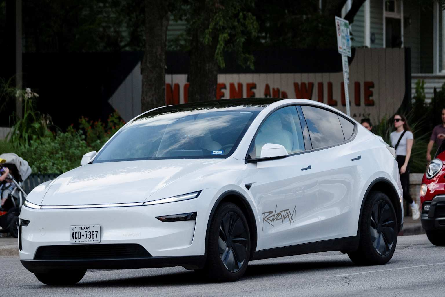 A white Tesla robotaxi with a Texas license plate on a street