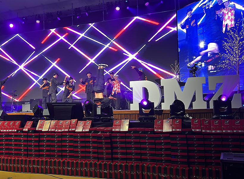 신한대학교 DMZ 어노인팅 축제 무대에서 갬블러크루(Gamblerz Crew)가 오렌지색 의상을 입고 브레이킹 퍼포먼스를 선보이는 장면. LED 조명과 대형 화면 속 역동적인 그래픽이 어우러진 화려한 무대 연출이 돋보인다.