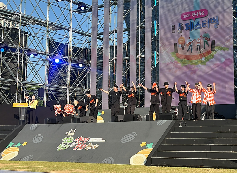 2024 경상북도 성주참외 & 생명문화축제 메인무대에서 갬블러크루(Gamblerz Crew) 댄서들이 스트릿댄스 퍼포먼스를 선보이며 인사하는 장면. 대형 LED 스크린과 철제 무대 구조물, 파란 하늘 아래 펼쳐진 야외 페스티벌의 활기찬 분위기가 돋보인다.