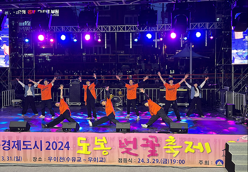 2024 도봉 벚꽃축제 메인무대에서 갬블러크루(Gamblerz Crew) 댄서들이 오렌지색 유니폼을 입고 스트릿댄스 퍼포먼스를 선보이는 장면. 무대 뒤로 화려한 조명과 LED 스크린이 빛나고, 많은 관객들이 봄밤 축제를 즐기고 있다.